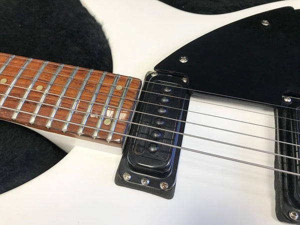 Close-up of white electric guitar neck and black single-coil pickup with metal frets and strings, featuring wooden fretboard with dot inlays and black pickguard.