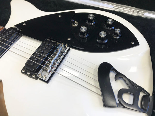 Close-up of white electric guitar body showing black pickguard with control knobs, single humbucker pickup, bridge, and black tailpiece on soft case lining