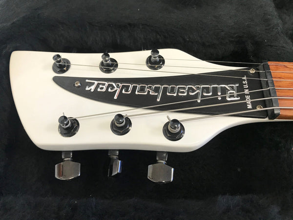 Close-up of white Rickenbacker electric guitar headstock with six tuning pegs and metal Rickenbacker logo plate, made in the USA, on a black background