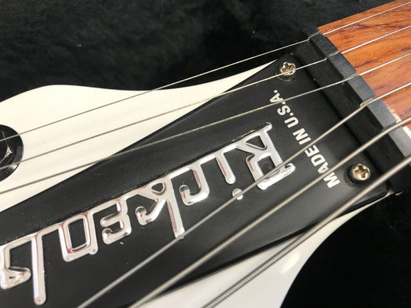 Close-up of a Rickenbacker guitar headstock with logo and "Made in U.S.A." text on black truss rod cover showing metal tuning strings and wooden neck