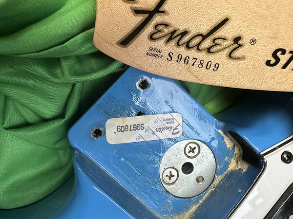 Close-up of Fender Stratocaster neck pocket showing serial number S967809 on blue guitar body with Fender neck label, highlighting guitar vintage and condition details.
