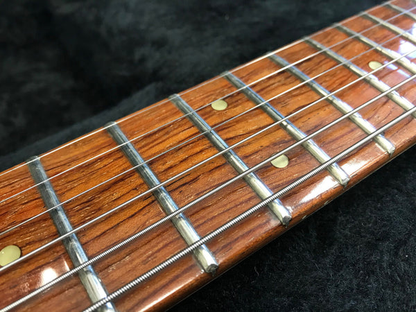 Close-up of guitar fretboard with metal frets and steel strings on polished wooden neck against black background