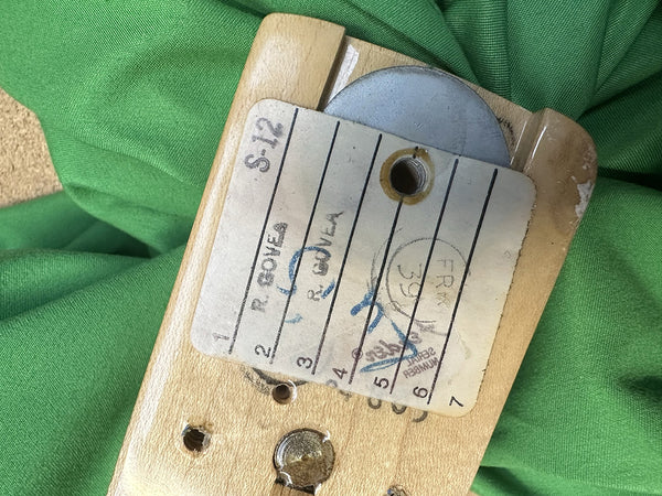 Close-up of a guitar neck heel with a worn inventory sticker labeled "S-12" and handwritten notes, photographed on a green fabric background for Coffee House Guitars product listing.