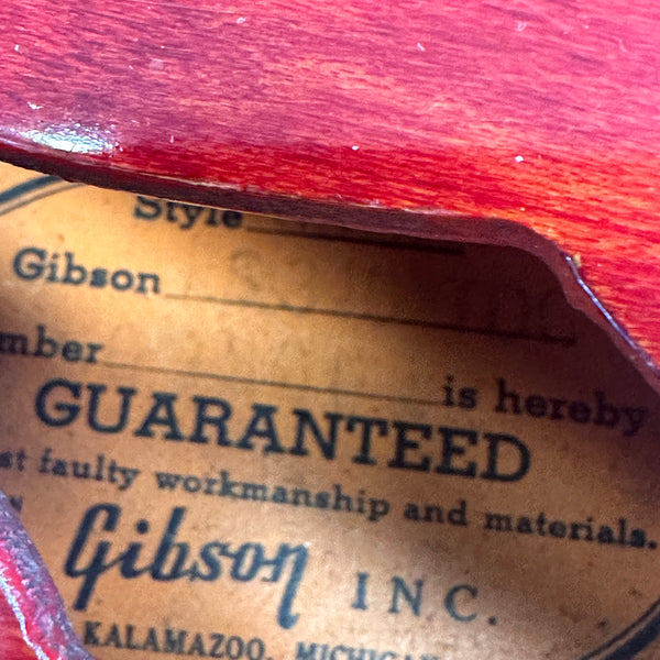 Close-up of vintage Gibson guitar label inside red wooden body, showing guarantee of workmanship and materials, made by Gibson Inc., Kalamazoo Michigan