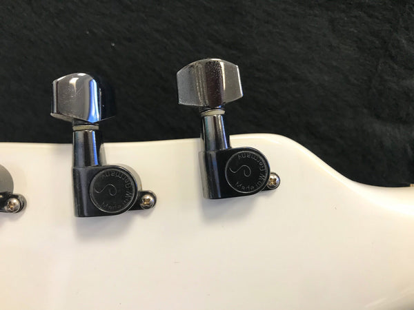 Close-up of chrome locking tuning pegs on white guitar headstock with black background