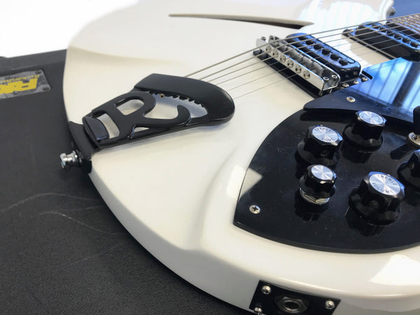 Close-up of white electric guitar tailpiece, bridge and black control knobs for treble, tone, and volume on black pickguard with guitar strings and output jack visible