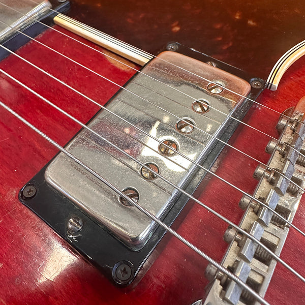 Close-up of vintage chrome electric guitar pickup and strings on red sunburst guitar body with adjustable bridge saddles