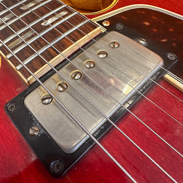 Close-up of vintage humbucker pickup, rosewood fretboard, and steel strings on red electric guitar body