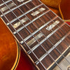 Close-up of vintage guitar fretboard with mother of pearl block inlays and metal frets, showing six wound steel strings on a sunburst finish body.