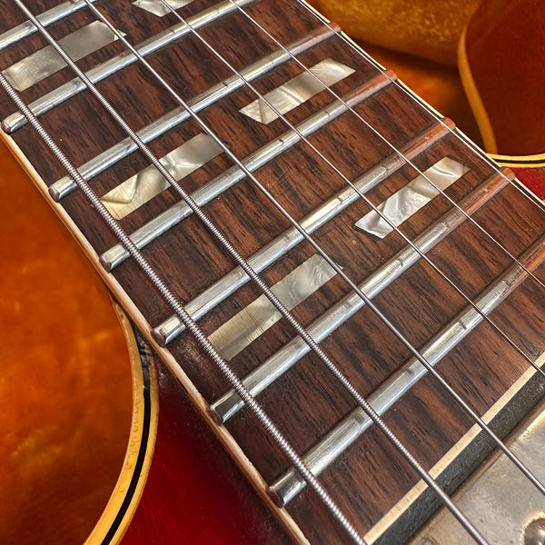 Close-up of vintage guitar fretboard with mother of pearl block inlays and metal frets, showing six wound steel strings on a sunburst finish body.