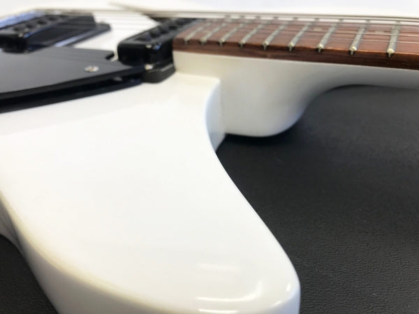 Close-up of white electric guitar body showing rosewood fretboard and black pickups on black background