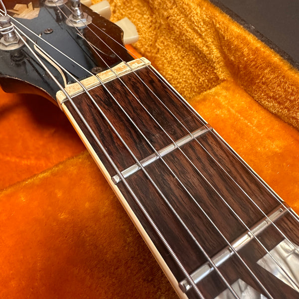 Close-up of guitar neck and fretboard with steel strings, lying in an orange plush guitar case interior