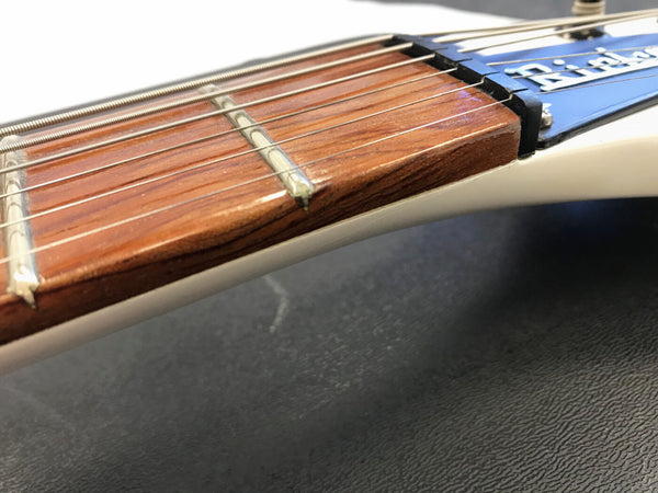 Close-up of electric guitar neck and strings showing rosewood fretboard and white guitar body on black textured surface