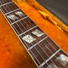 Close-up of guitar neck with mother of pearl diamond inlays and steel strings on rosewood fretboard, resting on orange plush guitar case lining.