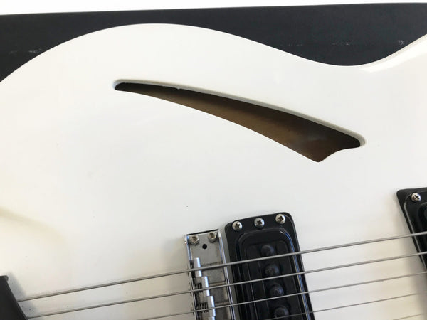 Close-up of white electric guitar body showing f-hole, bridge, and pickups with metal strings against black background