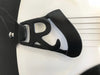 Close-up of black metal guitar tailpiece with cutout letter R on white guitar body and strings