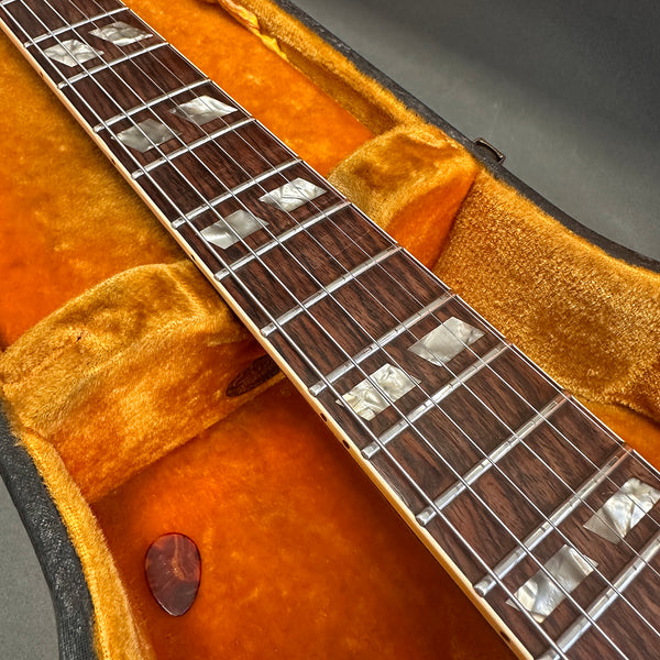 Close-up of guitar fretboard with mother-of-pearl inlays and steel strings inside plush orange velvet guitar case with guitar pick.