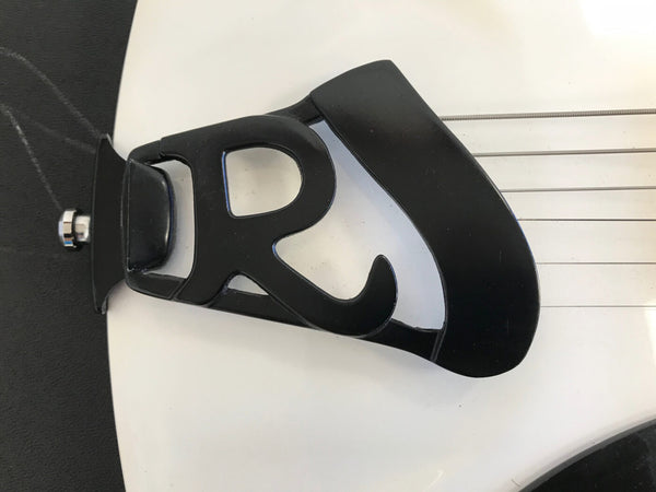 Close-up of black metal guitar tailpiece with cutout letter R on white guitar body and strings