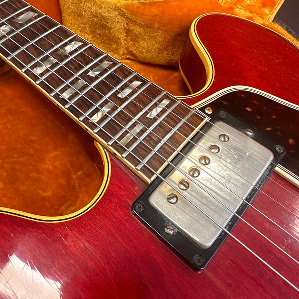Close-up of red electric guitar body and neck showing metal pickup, rosewood fretboard with mother-of-pearl trapezoid inlays, and vintage strings on orange guitar case interior