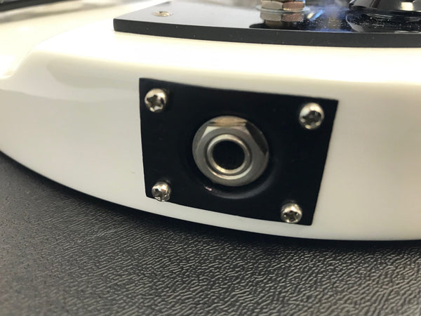 Close-up of electric guitar output jack on white guitar body with black jack plate and chrome screws on textured black surface