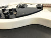 Close-up of white electric guitar body with black pickguard, control knobs, and pickup selector switch on textured black surface