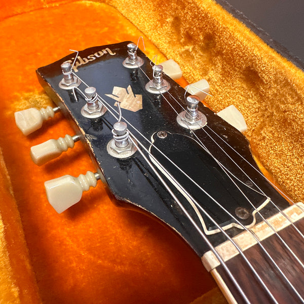 Close-up of vintage Gibson guitar headstock with tuning pegs and strings inside orange plush guitar case