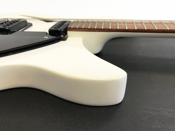 Close-up of white electric guitar body with black pickups and brown fretboard on black surface at Coffee House Guitars