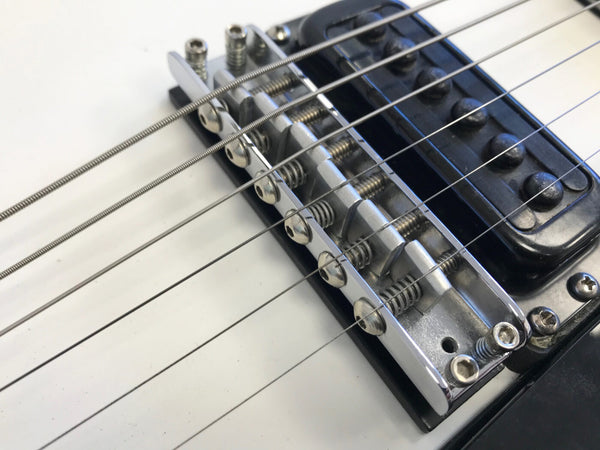 Close-up image of electric guitar bridge and strings with black pickup on white guitar body