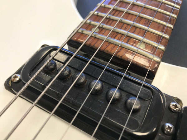 Close-up of electric guitar black pickup and fretboard with metal frets and strings on white guitar body