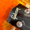 Close-up of Gibson guitar headstock with vintage logo and tuning pegs on orange plush background