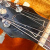 Close-up of vintage guitar headstock with tuning pegs, strings, and worn black finish on fretboard end in orange case interior