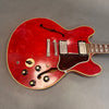 Close-up of vintage red semi-hollow body electric guitar with dual humbucker pickups, tortoiseshell pickguard, four black control knobs, and f-hole design, displayed on gray background
