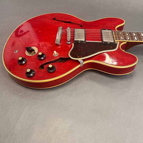 Red semi-hollow electric guitar with cream binding, chrome humbucker pickups, black control knobs, and tortoiseshell pickguard on grey background