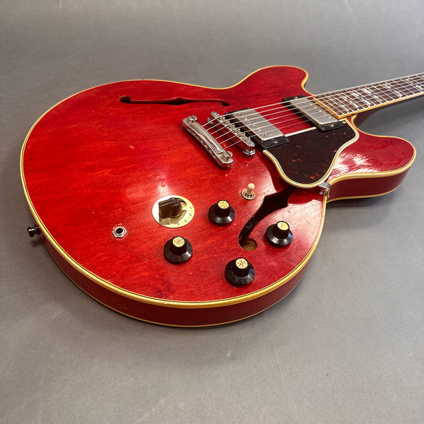 Red semi-hollow electric guitar with chrome bridge, black control knobs, cream binding, and tortoiseshell pickguard on gray background