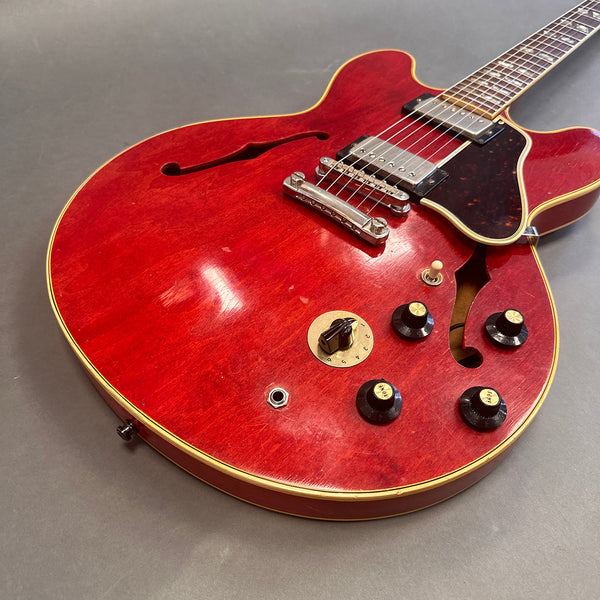 Close-up of red hollow body electric guitar with dual humbucker pickups, black control knobs, and cream binding on a gray background
