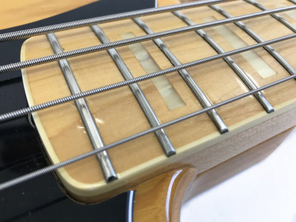 Close-up of maple fingerboard with rectangular inlays and metal frets on electric bass guitar strings