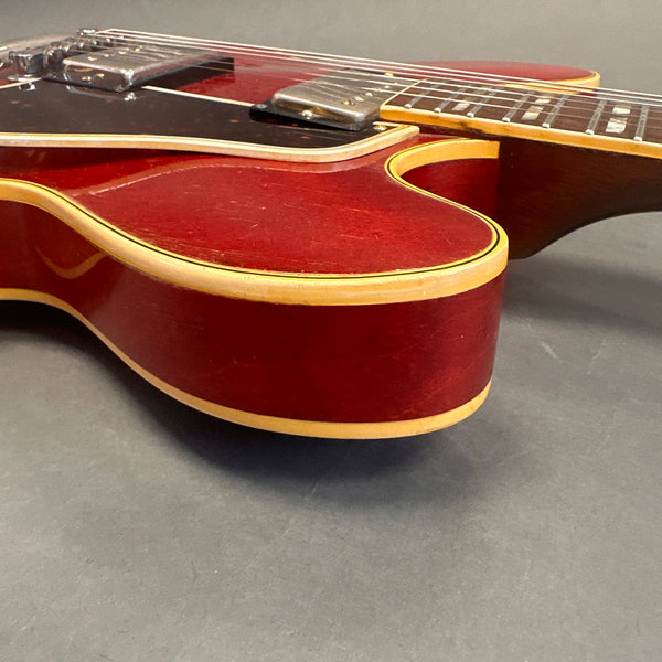 Close-up of vintage red hollow body electric guitar with cream binding and black pickguard on gray background