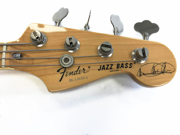 Fender Jazz Bass guitar headstock with tuning pegs and signature on natural wood finish, made in Japan, close-up of serial number and string winding.