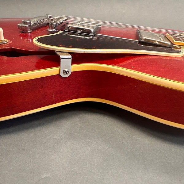 Close-up of red semi-hollow electric guitar body with cream binding and chrome hardware on gray background