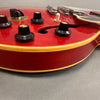 Close-up of red semi-hollow body electric guitar with black control knobs and cream binding on gray background