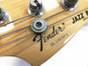 Close-up of Fender Jazz Bass guitar headstock showing tuning pegs, Fender logo, serial number S032013, and metal string retainer on natural wood finish