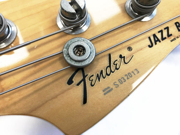 Close-up of Fender Jazz Bass guitar headstock showing tuning pegs, Fender logo, serial number S032013, and metal string retainer on natural wood finish