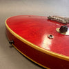 Close-up image of vintage red electric guitar body showing worn finish, cream binding, input jack, and control knob on gray background
