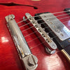 Close-up of red hollow body electric guitar bridge, tailpiece, and chrome covered pickups with guitar strings, showing vintage hardware details