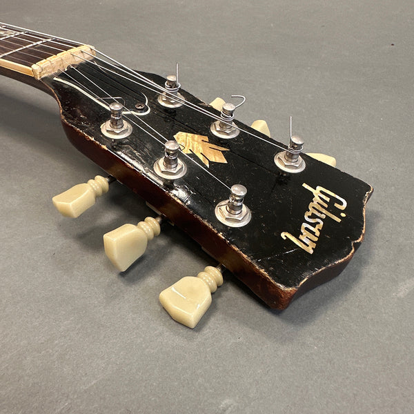 Close-up of vintage Gibson guitar headstock with cream tuning pegs and worn black finish on gray background