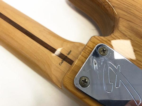 Close-up of guitar neck joint with "Crafted in Japan" text and chrome neck plate with engraved logo on natural wood finish electric guitar