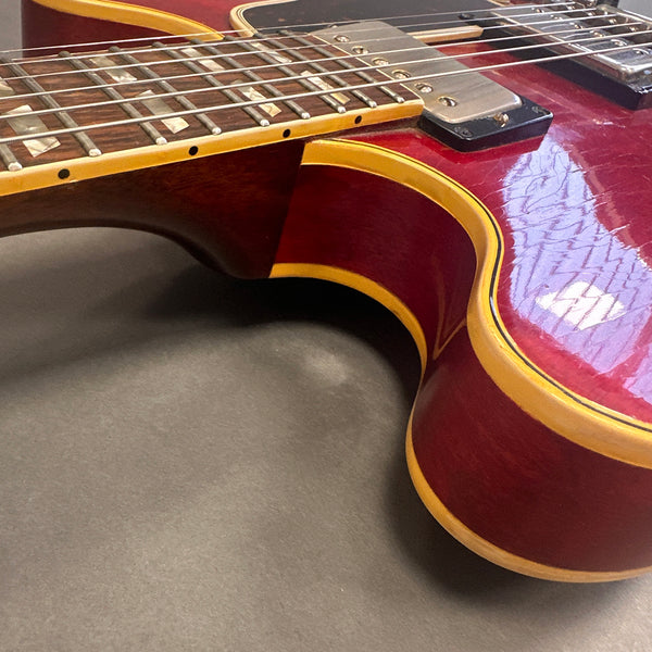 Close-up of red electric guitar body with cream binding and rosewood fretboard showing inlay dots and pickups on gray background