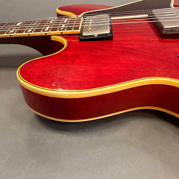 Close-up of red electric guitar body with cream binding and chrome humbucker pickups on gray background