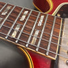 Close-up of rosewood guitar fretboard with rectangular pearloid inlays and metal frets on red electric guitar body with cream binding