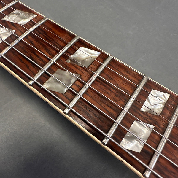 Close-up of guitar fretboard with diamond-shaped mother of pearl inlays and metal frets on a dark wooden neck